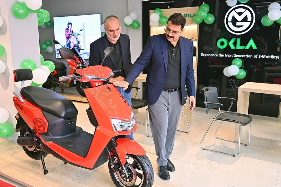 Corporate executives inspecting an OKLA electric scooter at an e-mobility showroom during a product launch event.